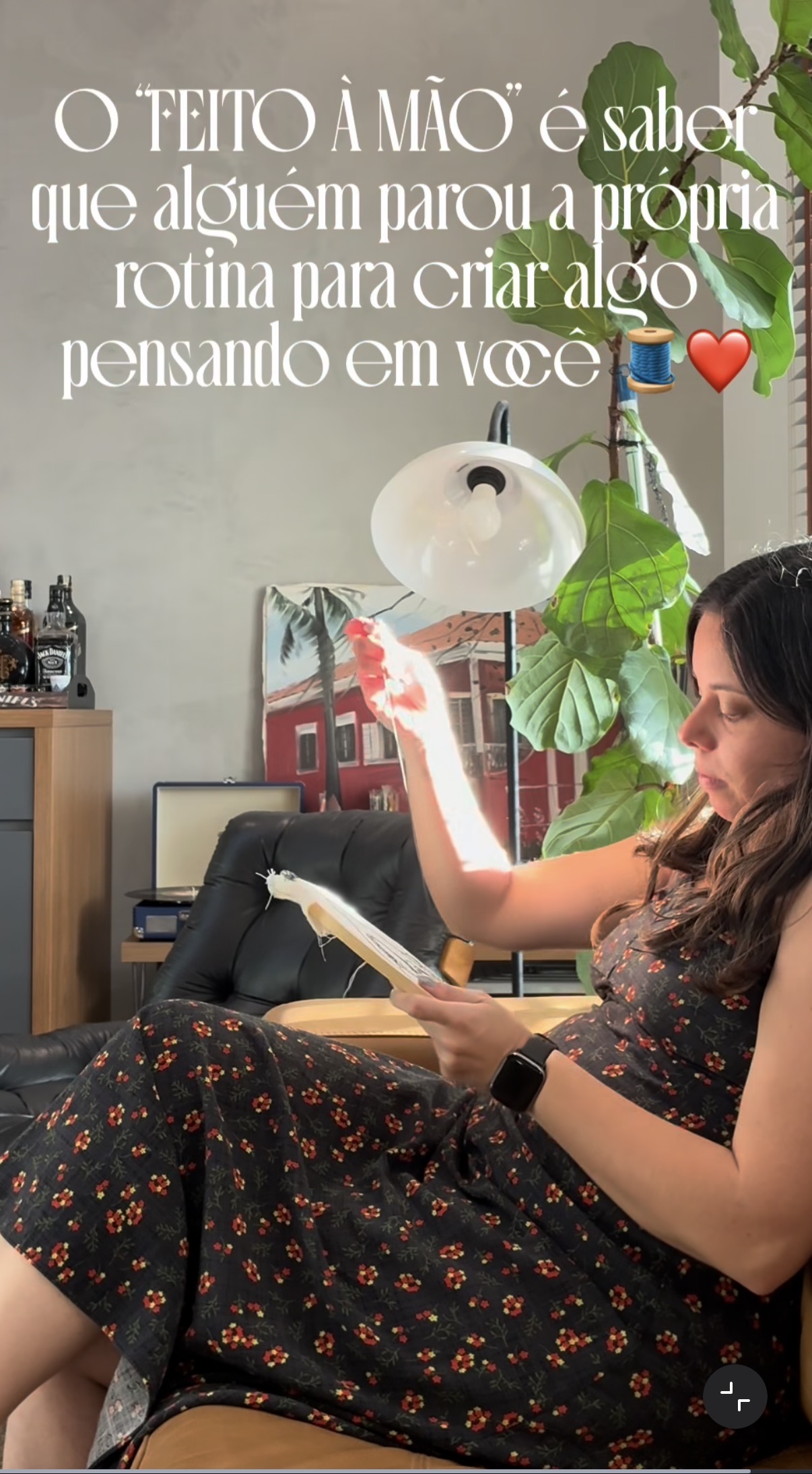 Joici bordando à mão, puxando a linha sobre o bastidor em um ambiente com plantas